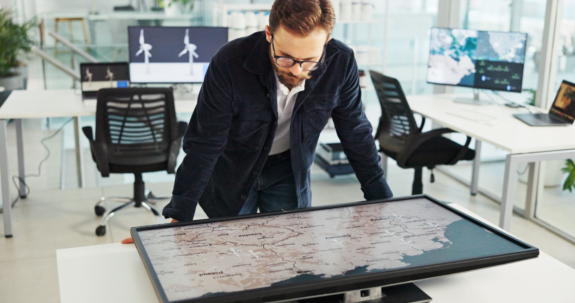 Hombre de negocios, pantalla interactiva y mapa en la oficina para la sostenibilidad, la energía limpia o la ubicación de turbinas eólicas. Global, mundial o trabajador con pantalla para la planificación de proyectos con especialista en energía renova